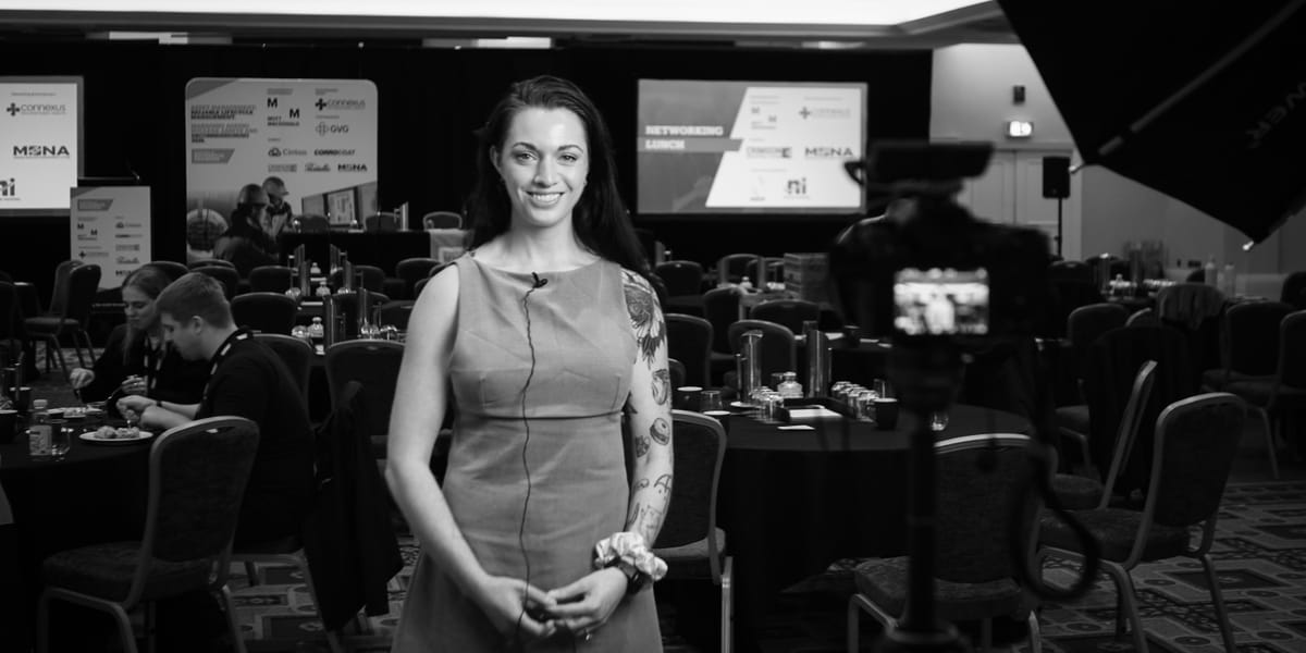 Black and white frame of a presenter being filmed at a conference networking lunch.