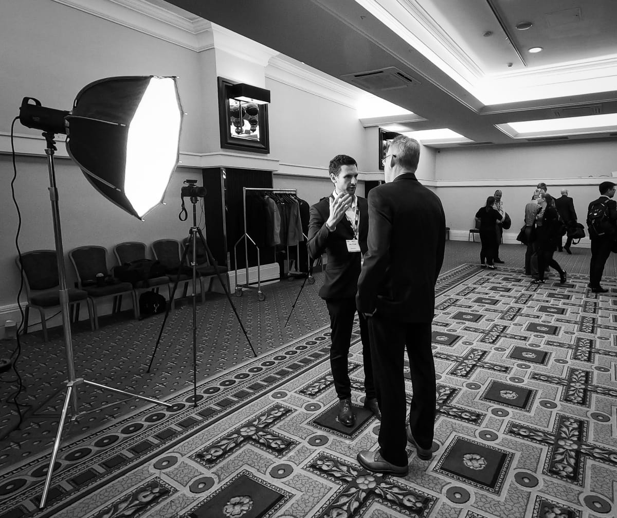 Black and white frame of a lighting and camera setup being prepared in a conference room.